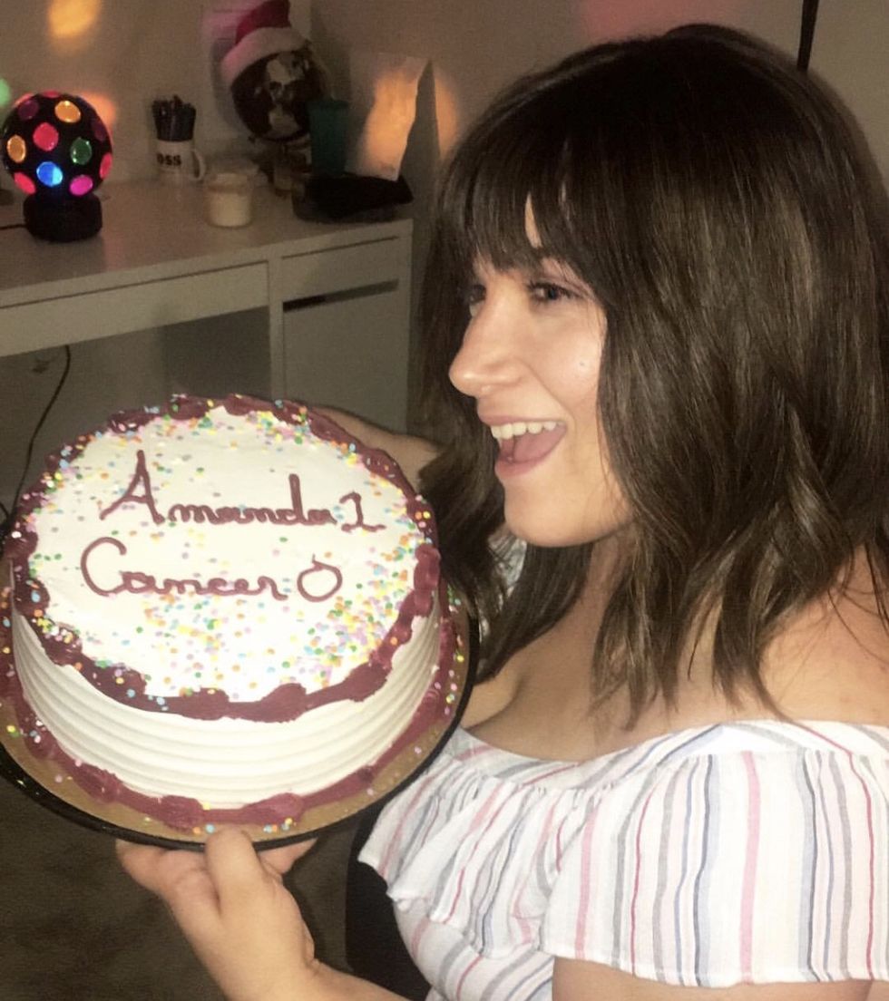 the author in a wig holding a cake that reads amanda 1 cancer 0