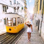 Woman tourist walking in narrow streets of Lisbon city old town. Famous retro yellow funicular tram on a sunny summer day. Tourist attraction.