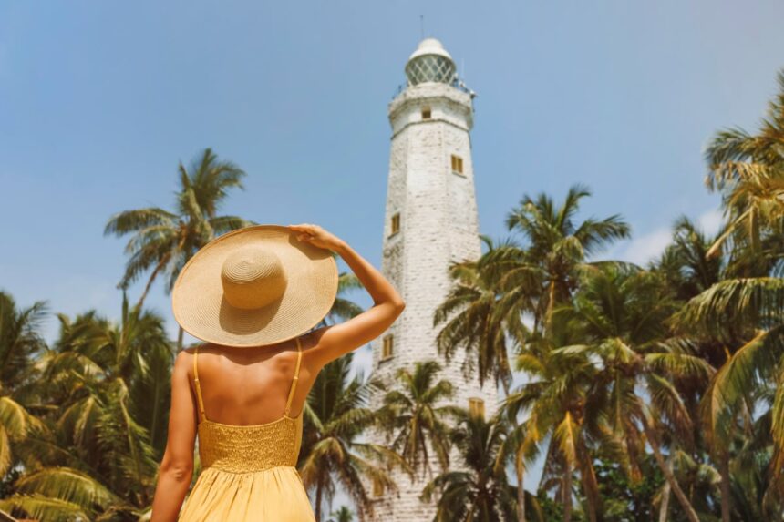 young female digital nomad traveler in a hat looks up at lighthouse in galle sri lanka