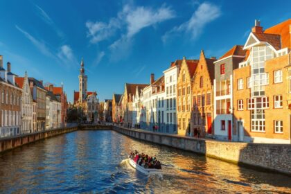 Tourist boat on canal Spiegelrei and Jan Van Eyck Square in the morning in Bruges, Belgium