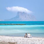 Couple sitting on beach along blue waters of Altea, Spain