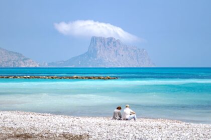 Couple sitting on beach along blue waters of Altea, Spain