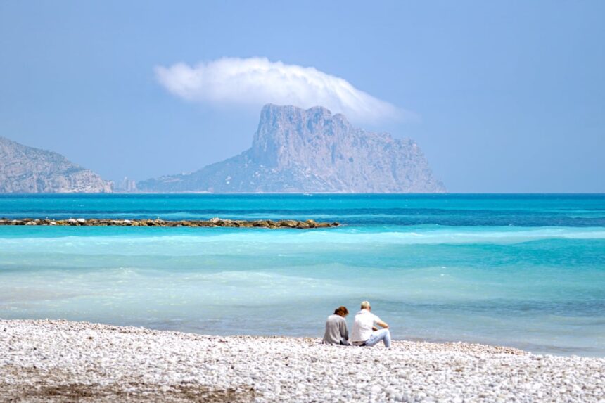 Couple sitting on beach along blue waters of Altea, Spain