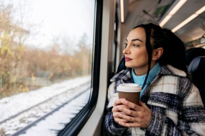 Woman with coffee riding train through snow