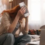oung Traveler Looking Confused As She Holds Her Passport, Using Her Computer