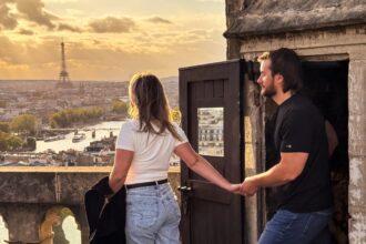 Man and woman walking out onto Parapet of a tower in Paris with the Eiffel Tower in the Background