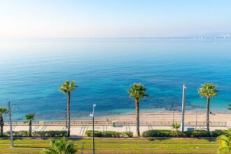 A woman sits alone on the sandy beach at the resort town of Palaio Faliro, Greece.