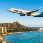 An Alaska Airlines Boeing 737 jet flying over Waikiki Beach and the Diamond Head volcanic cone in Honolulu, Hawaii.
