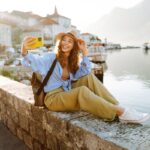 Pretty young girl enjoying the sunny weather on the viewpoint. Woman making selfie on smartphone for her stories in social network. Travelling as lifestyle.
