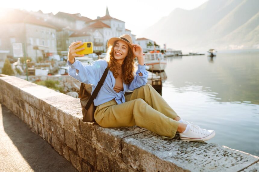 Pretty young girl enjoying the sunny weather on the viewpoint. Woman making selfie on smartphone for her stories in social network. Travelling as lifestyle.