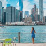 New York city Manhattan skyline seen from Brooklyn waterfront - woman enjoying view. American people walking enjoying view of Manhattan over the Hudson river from the Brooklyn side. NYC cityscape