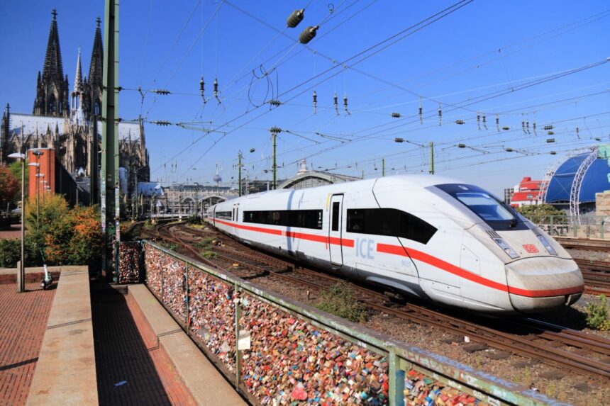 A white high-speed Deutsche Bahn ICE train passing the iconic Cologne Cathedral in Germany.