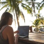 Digital nomad working on laptop under palm trees