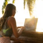 Digital nomad with laptop under palm tree