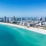 Miami Beach on blue sky. Skyline aerial view. Miami city. Tropical Miami scene. Miami district sky view. Famous oceanfront. Panoramic coastline. South beach panorama view. Summer holiday vibes.