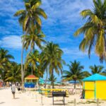 Caye Caulker Village, Caye Caulker, Belize Tourists walking along a sunny, palm tree lined beach pathway while enjoying colorful buildings in a small island town.