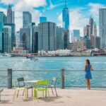 New York city Manhattan skyline seen from Brooklyn waterfront - woman enjoying view. American people walking enjoying view of Manhattan over the Hudson river from the Brooklyn side. NYC cityscape