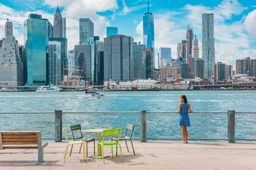 New York city Manhattan skyline seen from Brooklyn waterfront - woman enjoying view. American people walking enjoying view of Manhattan over the Hudson river from the Brooklyn side. NYC cityscape