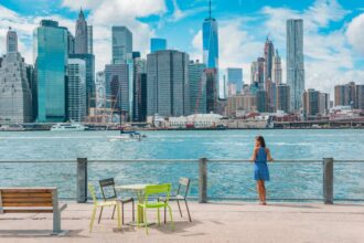 New York city Manhattan skyline seen from Brooklyn waterfront - woman enjoying view. American people walking enjoying view of Manhattan over the Hudson river from the Brooklyn side. NYC cityscape